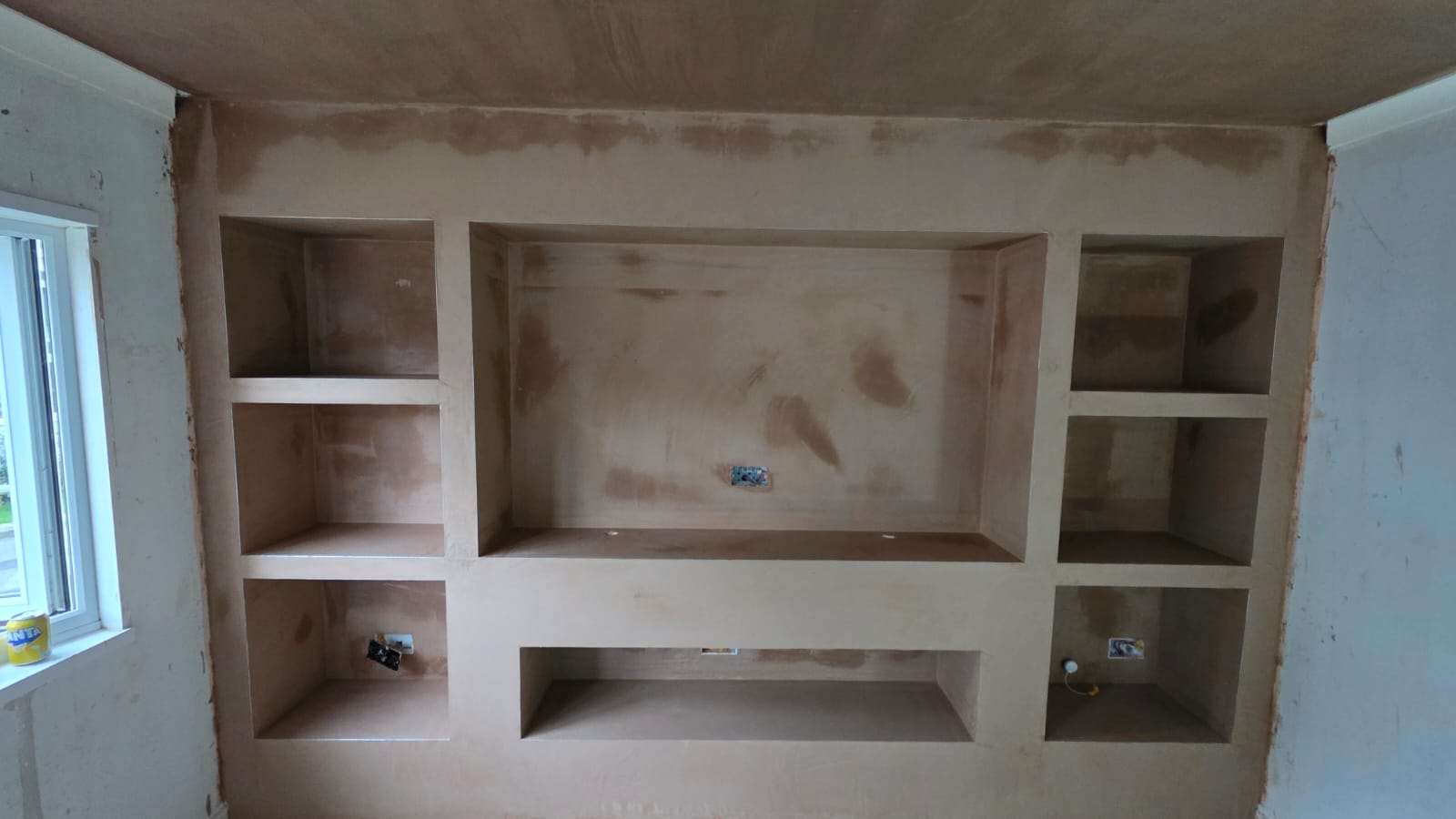 Bespoke plastered media wall with recessed shelving mid-build